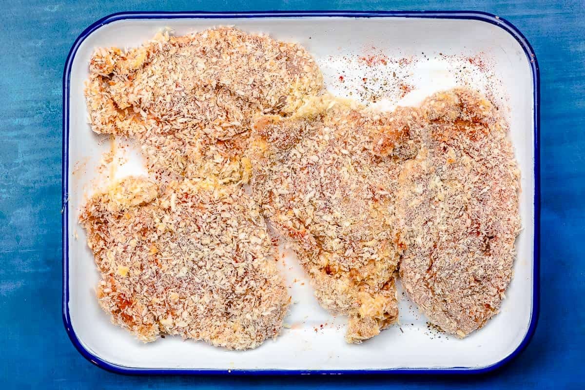 Uncooked chicken breasts coated in panko on a small sheet pan.