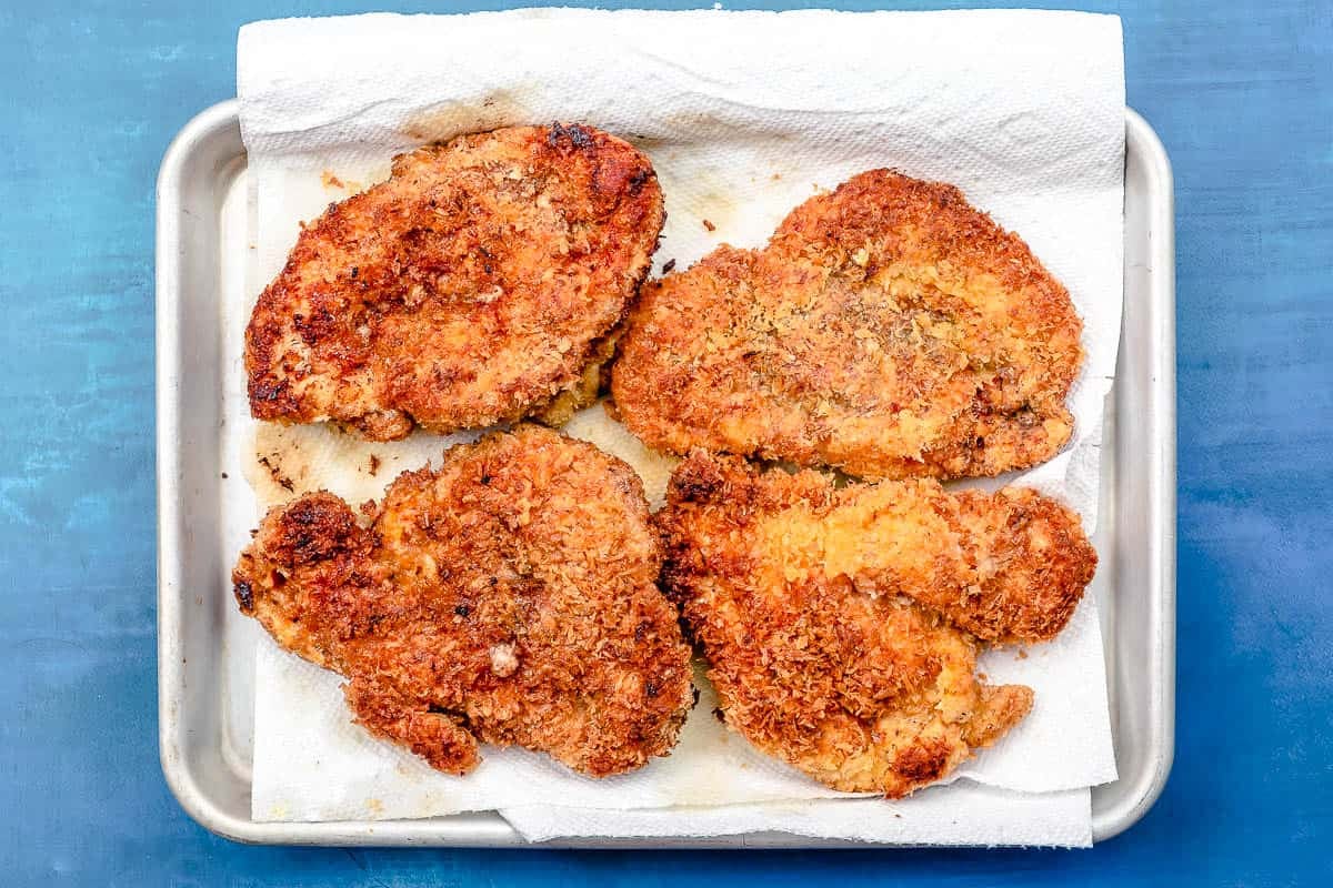 The freshly fried chicken schnitzel pieces on a paper towel lined sheet pan.
