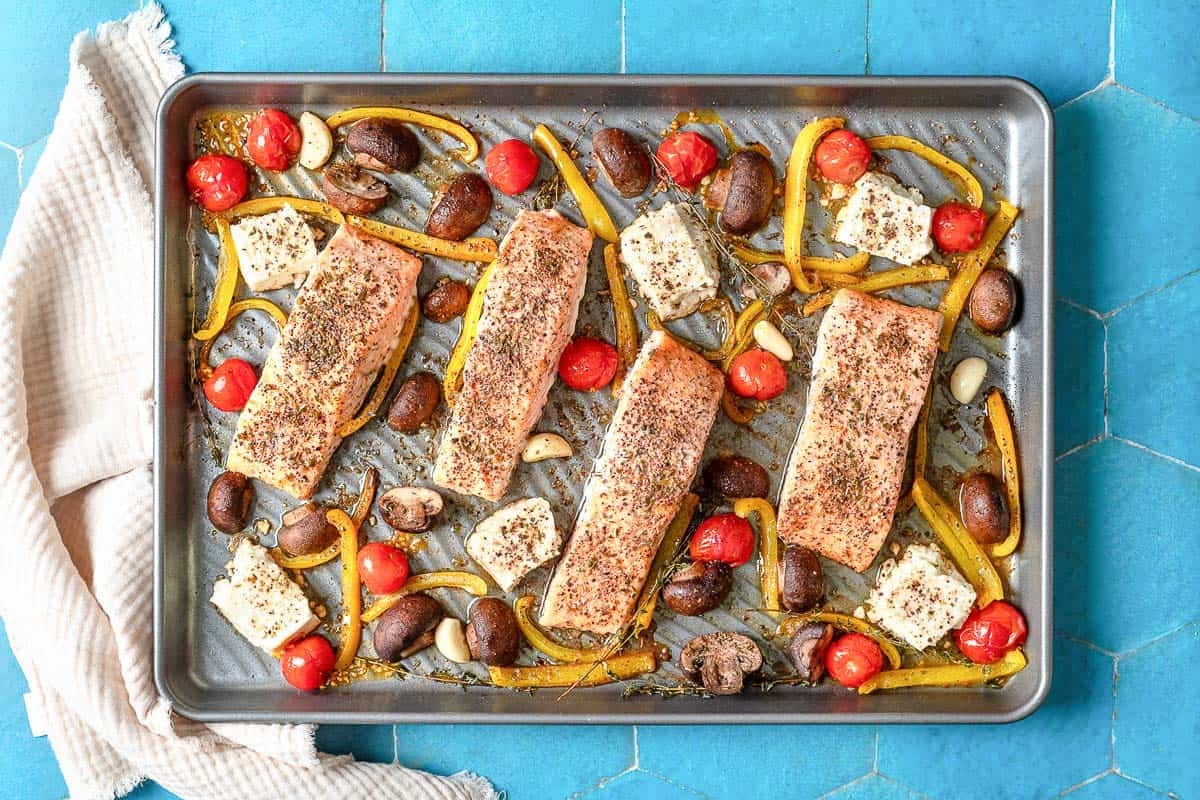 The mediterranean salmon recipe on a sheet pan next to a kitchen towel.