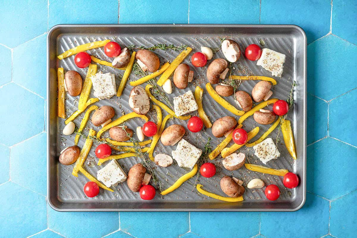 The unbaked vegetables and seasonings for the Mediterranean salmon recipe on a sheet pan.