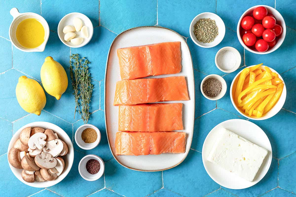 Ingredients for the Mediterranean salmon recipe including 4 salmon filets, a yellow bell pepper, baby bella mushrooms, garlic, cherry tomatoes, dried oregano, sumac, cumin, fresh thyme, lemons, feta cheese, salt and black pepper.
