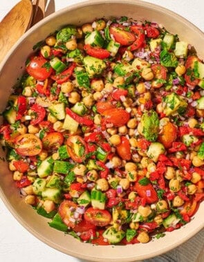 An overhead photo of the chickpea salad in a serving bowl next to a wooden serving spoon and fork, a jar of dijon dressing, and a cloth napkin.