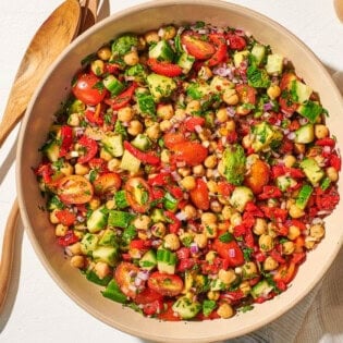 An overhead photo of the chickpea salad in a serving bowl next to a wooden serving spoon and fork, a jar of dijon dressing, and a cloth napkin.