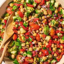 An overhead photo of chickpea salad in a serving bowl with a wooden serving spoon and fork.