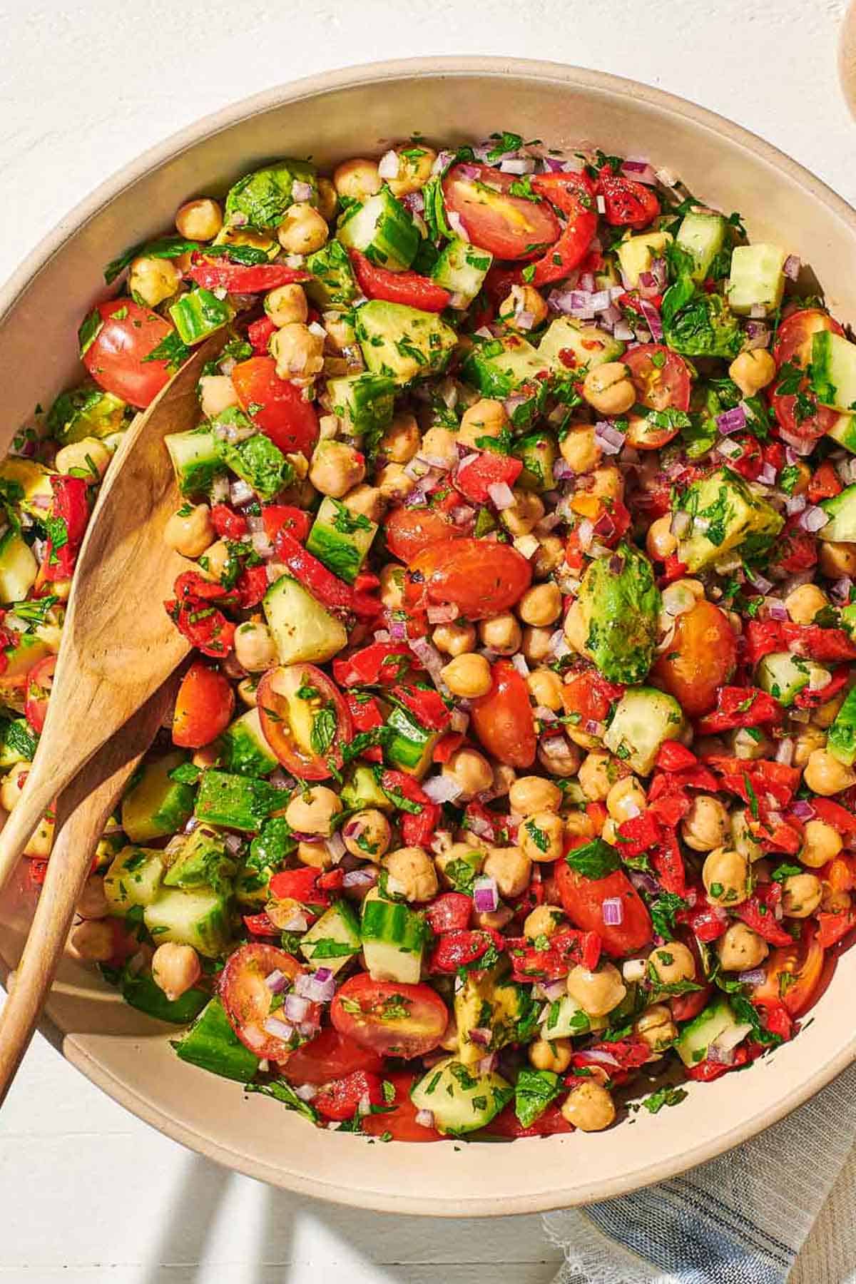 An overhead photo of chickpea salad in a serving bowl with a wooden serving spoon and fork.