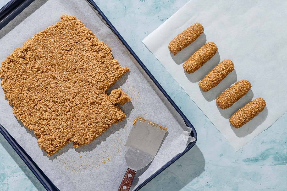 Five shaped alfajores on a piece of parchment paper. Next to this is the rest of the dough spread out on a parchment lined sheet pan with a spatula.