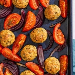 The baked chicken meatballs, tomatoes and red onions on a sheet pan.