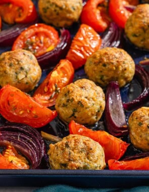 The baked chicken meatballs, tomatoes and red onions on a sheet pan.