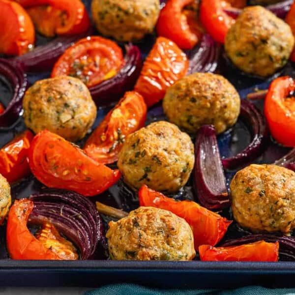 The baked chicken meatballs, tomatoes and red onions on a sheet pan.