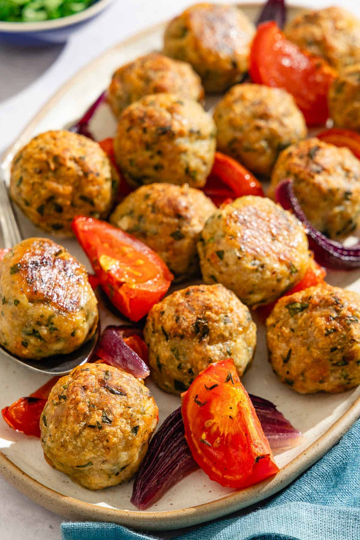 The baked chicken meatballs and veggies on a platter with a spoon.