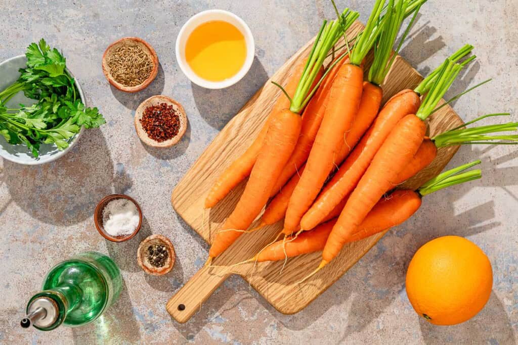 Ingredients for honey roasted carrots including carrots, an orange, honey, cumin seeds, olive oil, aleppo pepper, salt, black pepper and parsley.