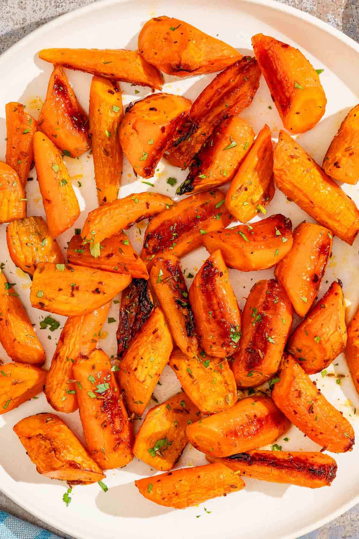 Honey roasted carrots topped with chopped parsley on a patter.