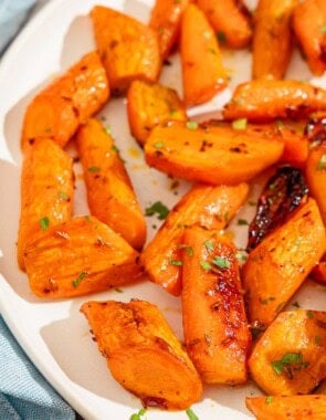 A close up of honey glazed carrots topped with chopped parsley on a platter.