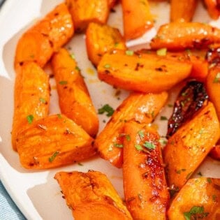 A close up of honey glazed carrots topped with chopped parsley on a platter.
