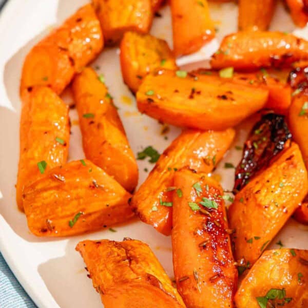 A close up of honey glazed carrots topped with chopped parsley on a platter.