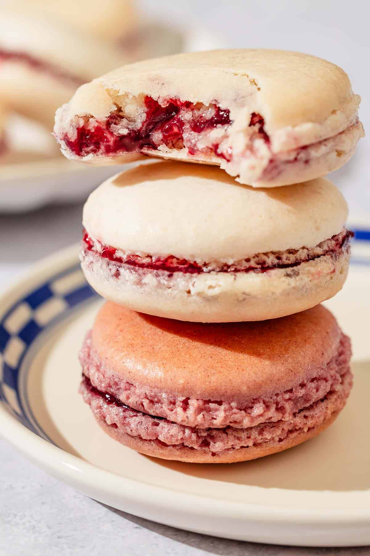 A stack of 3 macarons on a plate. The top one has a bite taken from it.
