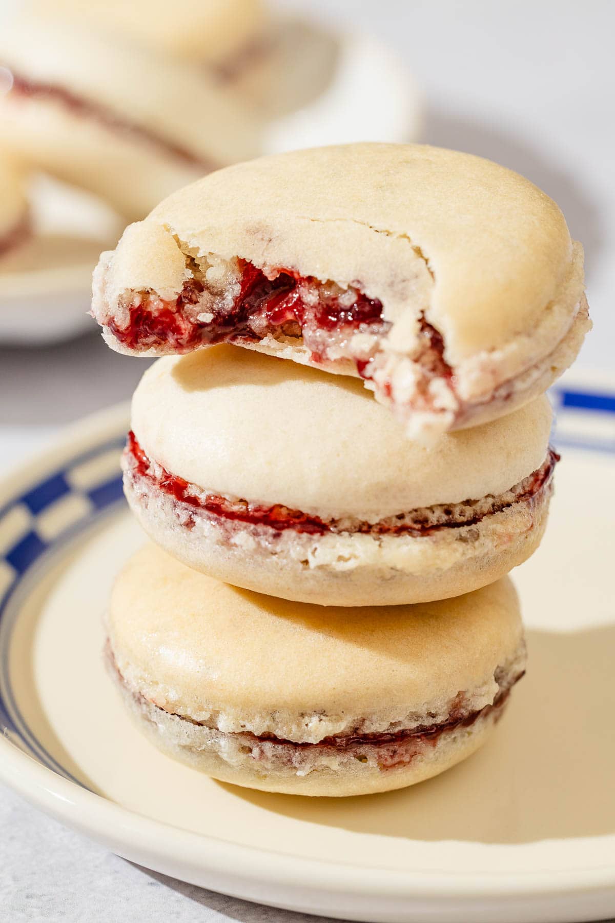 A stack of 3 macarons on a plate. The top one has a bite taken from it.