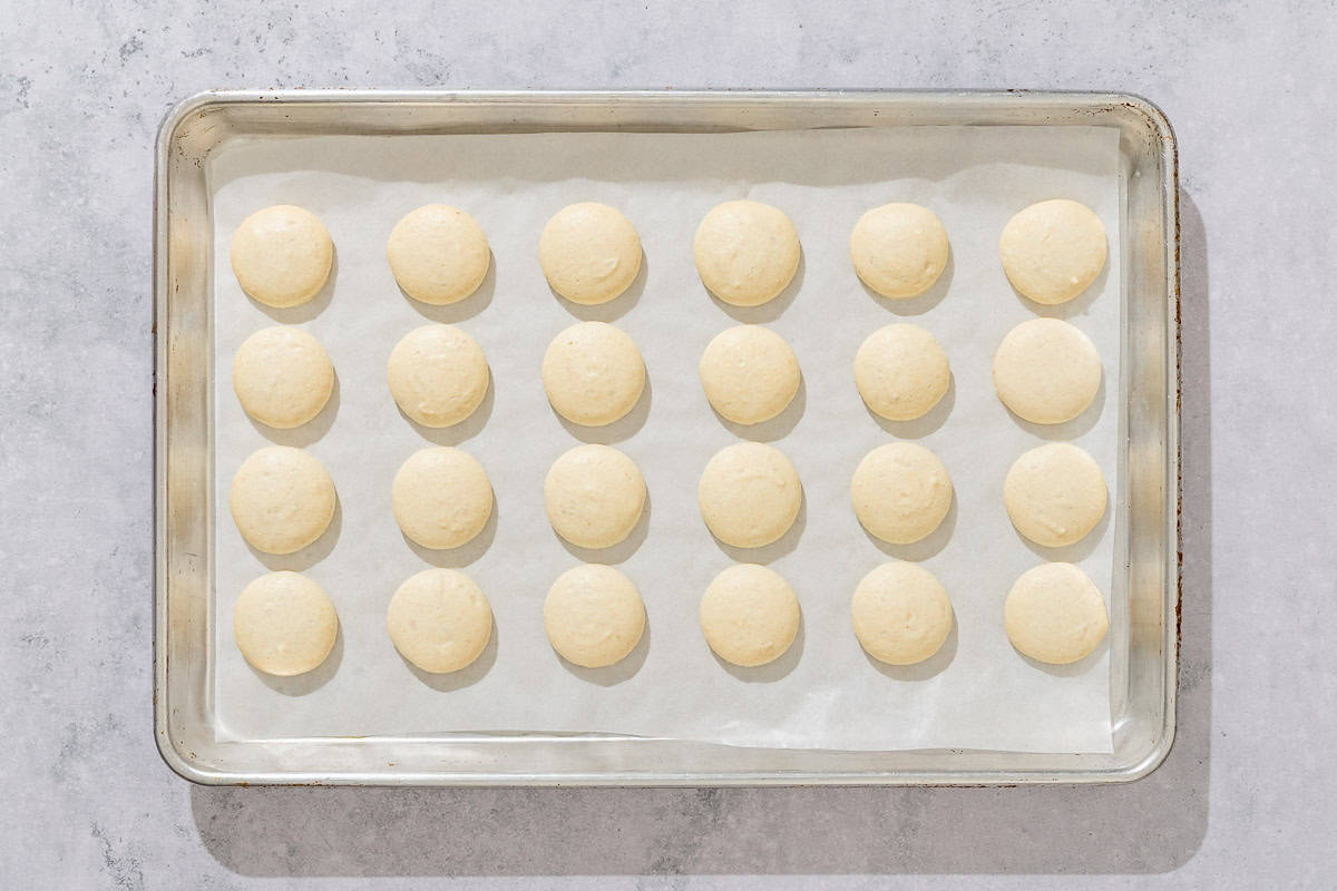 The unbaked macaron shells on a parchment lined sheet pan.