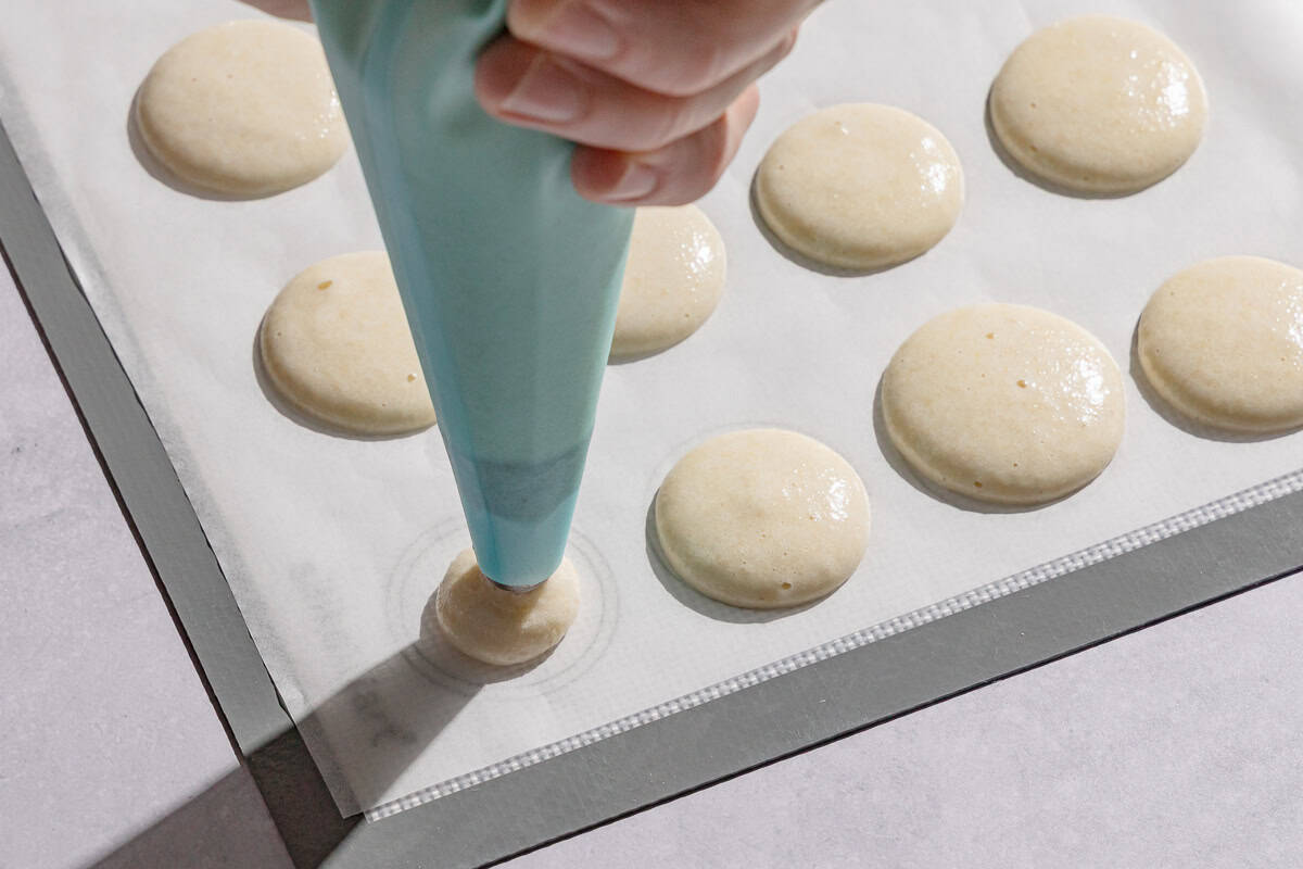 The macaron shells being piped onto a parchment lined macaron baking mat.