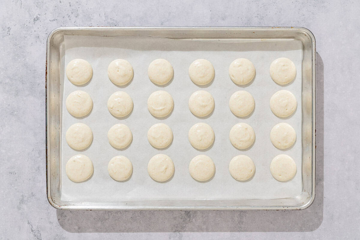 The unbacked macaron shells on a parchment line sheet pan.