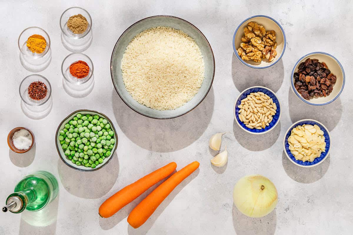 Ingredients for the rice pilaf recipe including rice, olive oil, onion, garlic, peas, carrots, salt, coriander, paprika, aleppo pepper, turmeric, walnuts, pine nuts, almonds, and raisins.