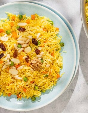 Rice pilaf on a plate with a fork. Next to this is the rest of the rice pilaf recipe in a skillet with a wooden spoon.