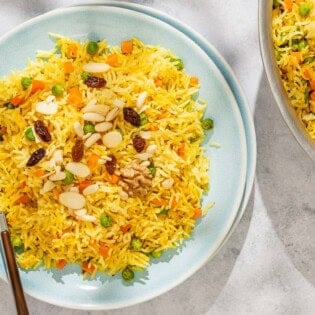 Rice pilaf on a plate with a fork. Next to this is the rest of the rice pilaf recipe in a skillet with a wooden spoon.