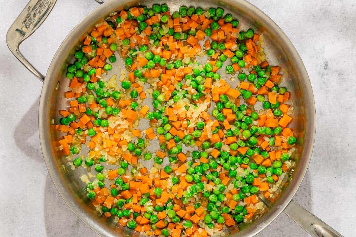 The onions, garlic, peas and carrots for the rice pilaf recipe being cooked in a skillet.
