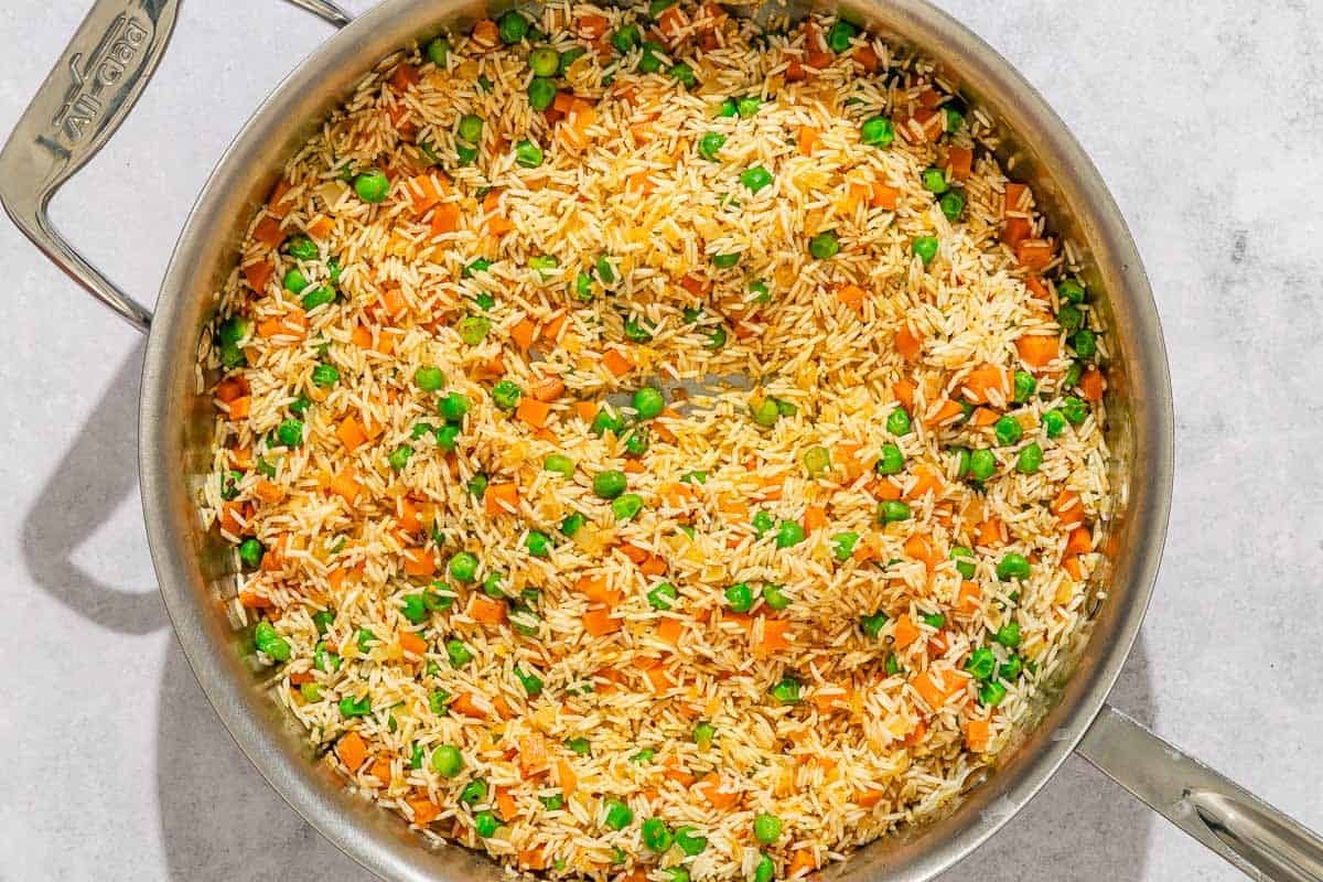 The onions, garlic, peas, carrots and rice for the rice pilaf recipe being cooked in a skillet.