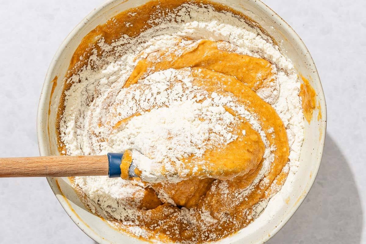 The dry ingredients for the persimmon bred being added to the wet ingredients in a bowl with a spatula.