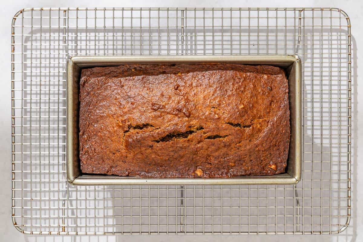 The baked loaf of persimmon bread in a loaf pan cooling on a wire rack.