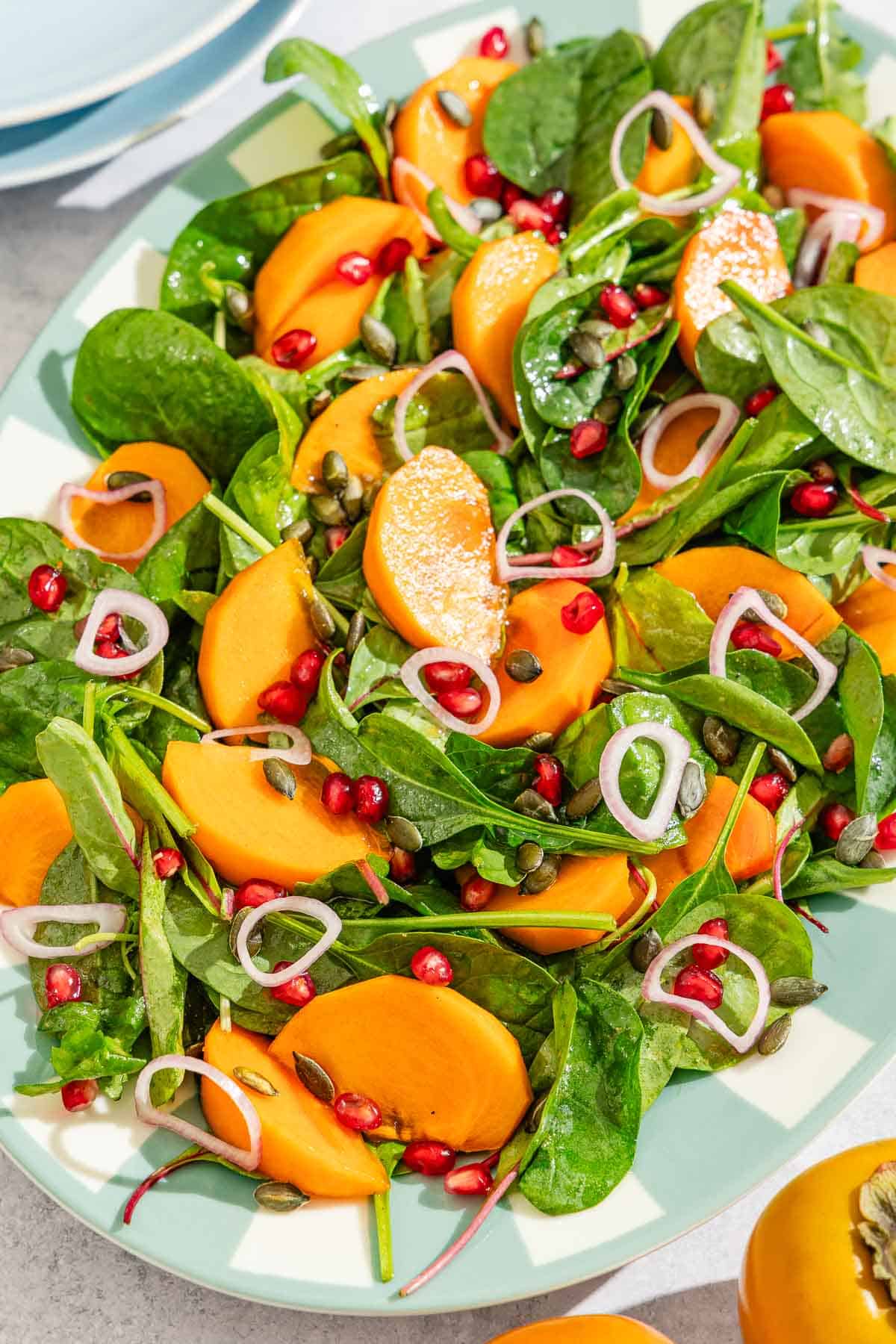 Persimmon salad on a platter next to a stack of 2 plates, and 2 persimmons.