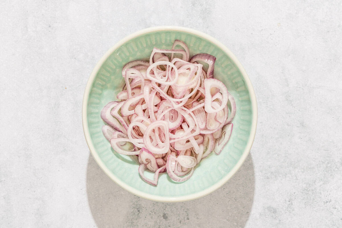 An overhead photo of a bowl of sliced shallots.