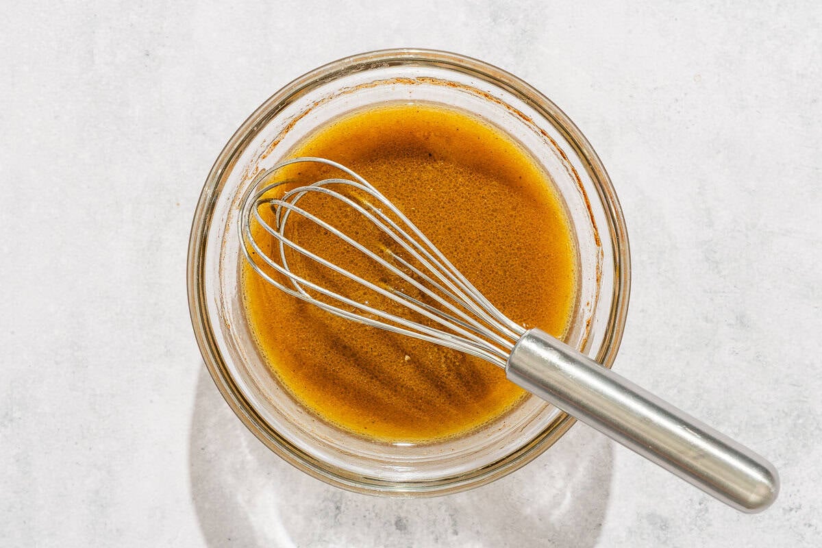 The dressing for the persimmon salad in a bowl with a whisk.