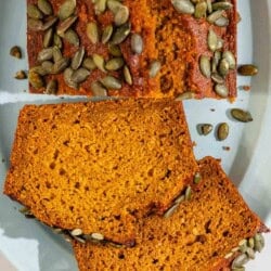 An overhead photo of a partial pumpkin bread loaf along with 2 slices on a platter.