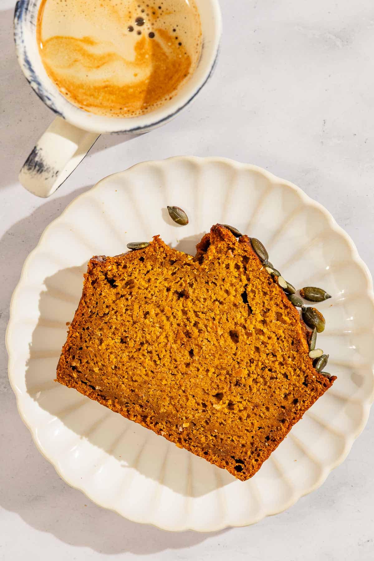 A slice of pumpkin bread on a plate next to a cup of coffee.