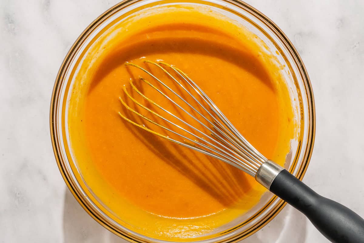 The wet ingredients for the pumpkin bread in a bowl with a whisk.