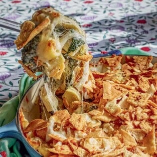 A spoonful of the spinach artichoke pasta being held over the rest of the pasta in a skillet.