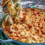 A spoonful of the spinach artichoke pasta being held over the rest of the pasta in a skillet.