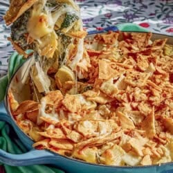 A spoonful of the spinach artichoke pasta being held over the rest of the pasta in a skillet.