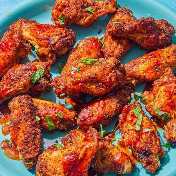 Air fryer chicken wings topped with harissa hot honey and chopped parsley on a platter. Next to this is a bowl of creamy feta dressing.