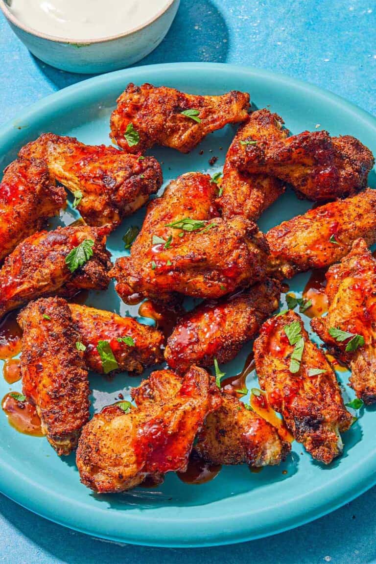 Air fryer chicken wings topped with harissa hot honey and chopped parsley on a platter. Next to this is a bowl of creamy feta dressing.