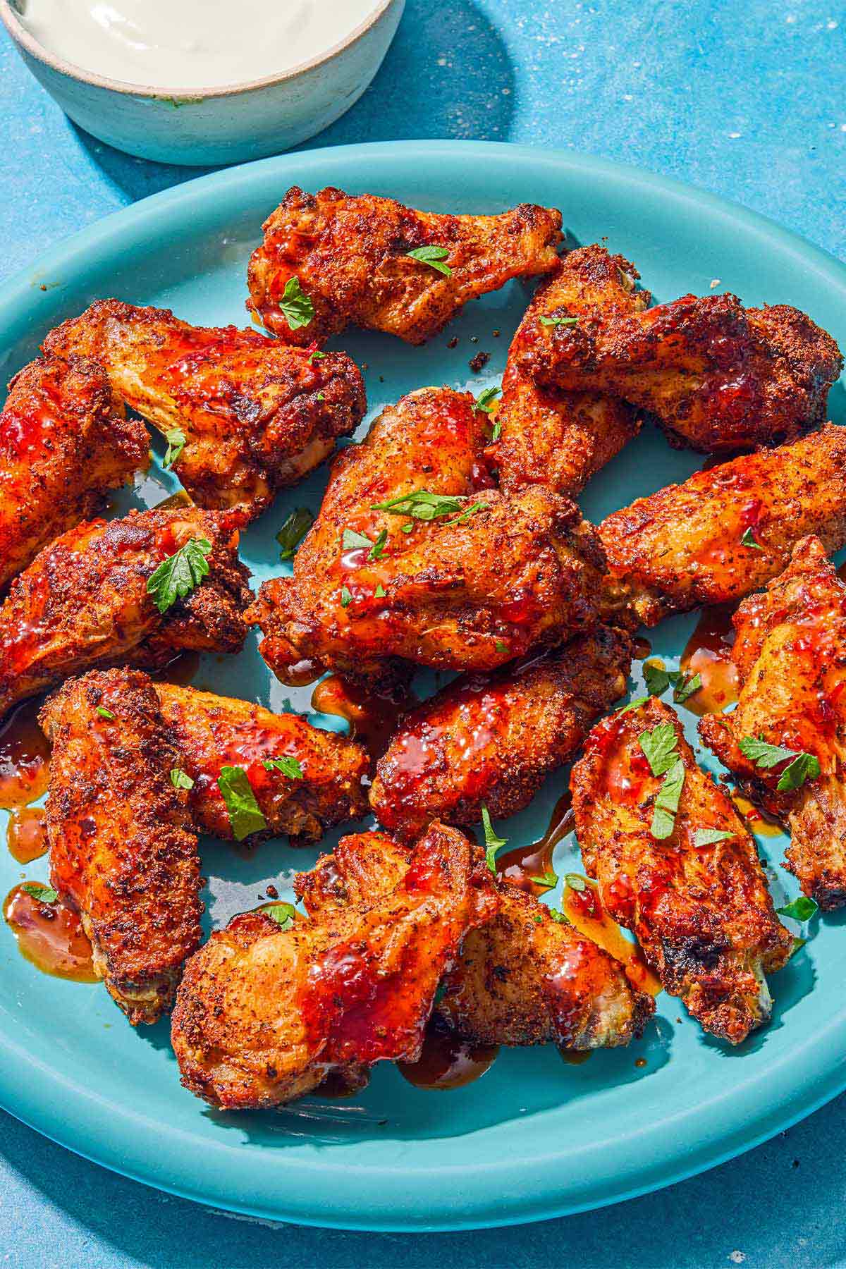 Air fryer chicken wings topped with harissa hot honey and chopped parsley on a platter. Next to this is a bowl of creamy feta dressing.