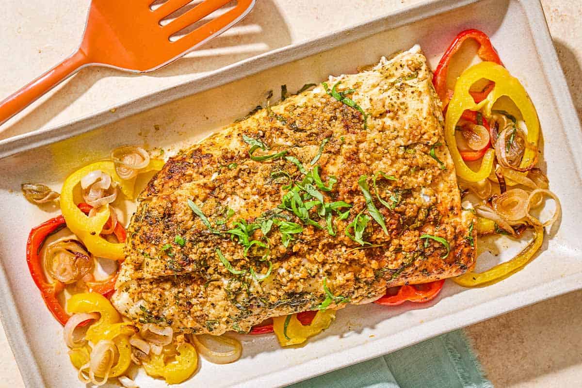 The baked fish recipe on a bed of peppers and shallots on a platter. Next to this is a spatula.
