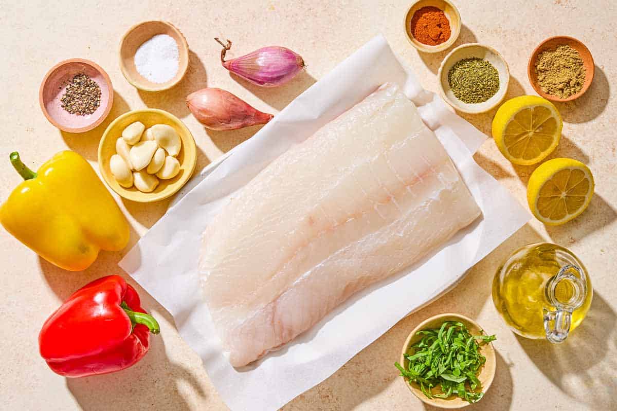 Ingredients for the baked fish recipe including a white fish fillet, salt, pepper, dry oregano, coriander, paprika, garlic, basil, olive oil, lemon, bell peppers, and shallots.