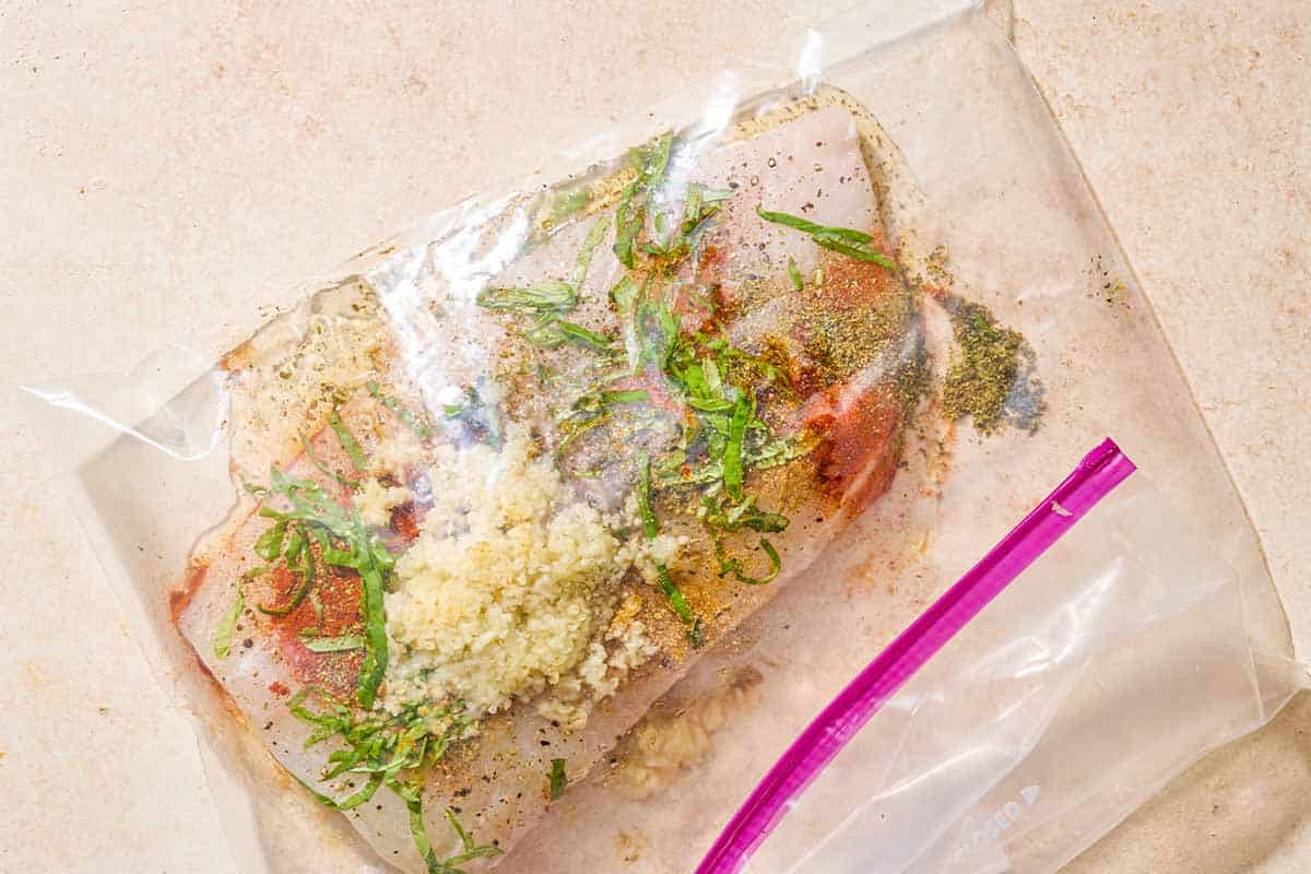 The white fish fillet being marinated in a zip top bag.