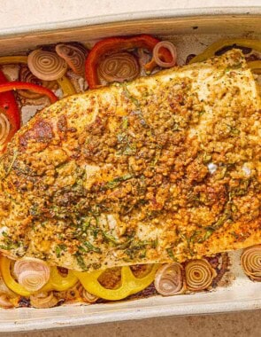 The baked fish recipe on a bed of peppers and shallots in a baking dish.