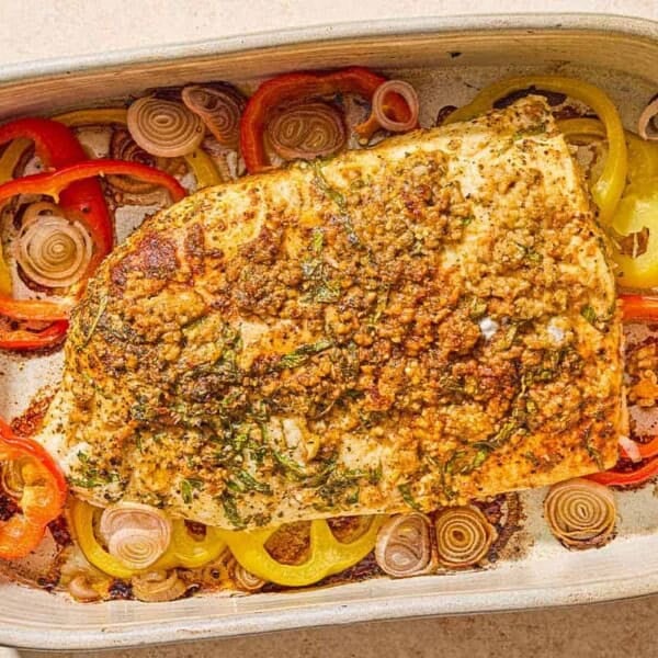 The baked fish recipe on a bed of peppers and shallots in a baking dish.
