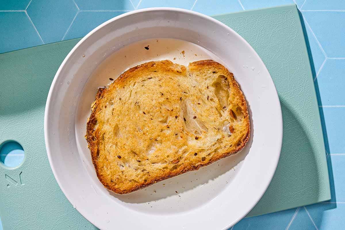 A slice of toasted bread in a bowl of water resting on a cutting board.