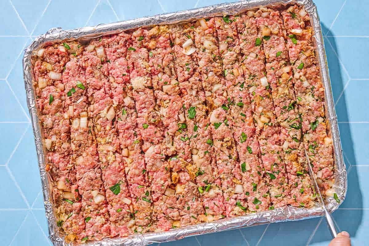 The unbaked sheet pan kofta being sliced on a foil lined sheet pan.